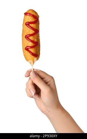 Woman holding delicious deep fried corn dog with ketchup on white background, closeup Stock Photo