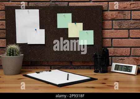 Corkboard with pinned notes hanging on brick wall over desk in office Stock Photo