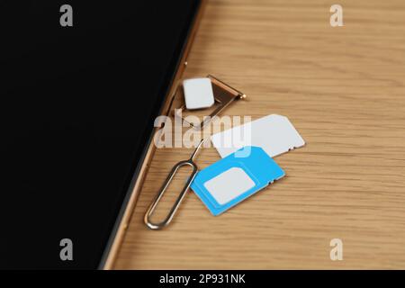 SIM cards, mobile phone and ejector tool on wooden table, closeup Stock Photo