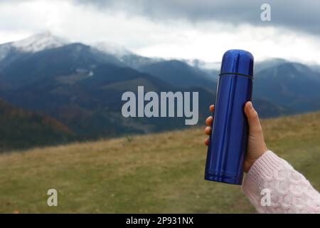 Woman holding blue thermos in mountains, closeup. Space for text Stock Photo