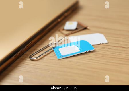 SIM cards, mobile phone and ejector tool on wooden table, closeup Stock Photo
