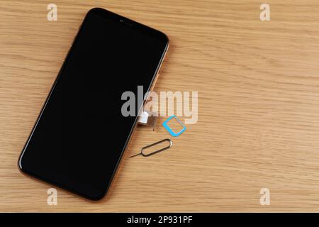 Mobile phone with SIM card in tray and ejector tool on wooden table, flat lay. Space for text Stock Photo