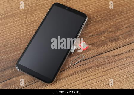 SIM card, mobile phone and ejector tool on wooden table Stock Photo