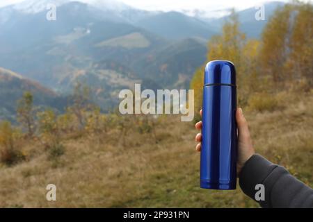 Woman holding blue thermos in mountains, closeup. Space for text Stock Photo
