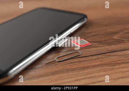 Mobile phone, SIM card and ejector tool on wooden table, closeup Stock Photo