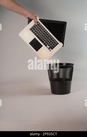 Electronic waste, broken or damaged, laptop in the trash, on a gray background and empty space or copy space, reuse and recycling concepts. Human hand, horizontal photo. Stock Photo