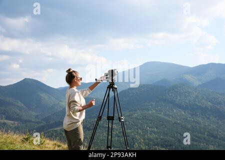 Professional photographer with modern camera on tripod in mountains. Space for text Stock Photo
