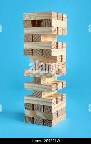 Jenga tower made of wooden blocks on light blue background Stock Photo