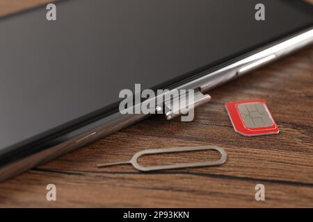 SIM card, mobile phone and ejector tool on wooden table, closeup Stock Photo