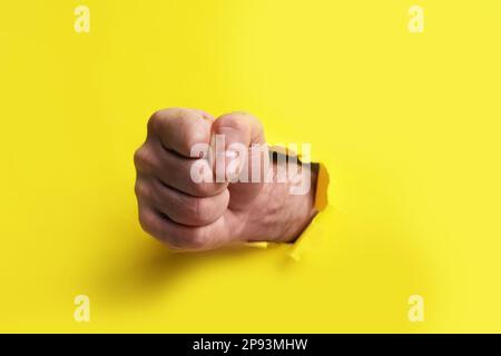 Man breaking through yellow paper with fist, closeup Stock Photo