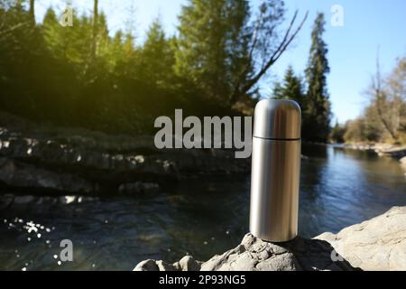 https://l450v.alamy.com/450v/2p93ng5/thermos-on-rock-near-mountain-river-outdoors-space-for-text-2p93ng5.jpg