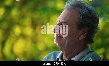 A thoughtful senior man sitting outside at park in deep contemplation. Candid close up of a pensive mature older person in nature Stock Photo
