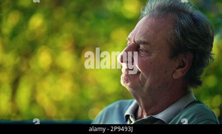 A thoughtful senior man sitting outside at park in deep contemplation. Candid close up of a pensive mature older person in nature Stock Photo