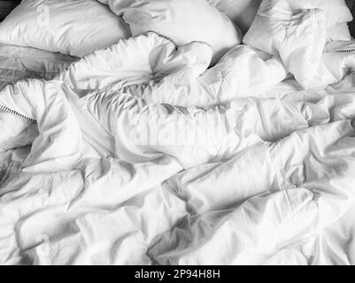 Domestic background of the rumpled duvet cover, white sheets and pillows on a bed. Stock Photo