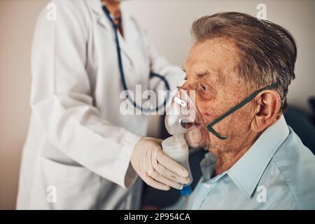 Doctor applying a medicine during inhalation to senior man suffering from lung disease. Covid-19 or coronavirus treatment. Doctor's home visiting duri Stock Photo