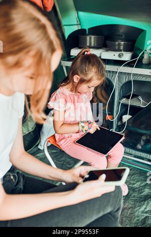 Sisters spending family time in a tent on camping. Children using tablet playing games online during summer vacation Stock Photo