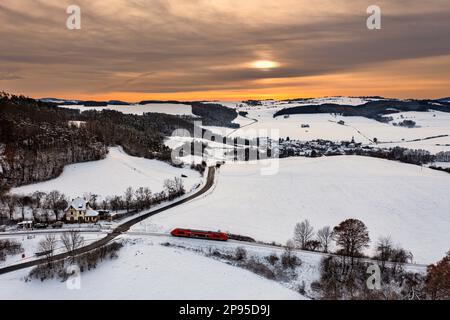 Germany, Thuringia, Bechstedt, Allendorf (background), regional train 60, train 29886, stop, house (former reception building), landscape, village, fields, forests, snow, overview, sunset shimmers through the clouds, back light Stock Photo