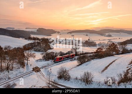 Germany, Thuringia, Allendorf, regional train 60, train 29889, level crossing, landscape, village, fields, forests, snow, overview, evening light, back light Stock Photo