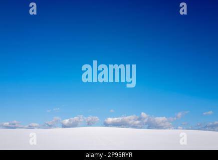 Snow covered field with few clouds and clear blue sky. Stock Photo
