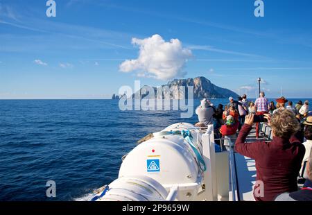 Approaching Capri by boat. Passengers on scheduled boat service from Amalfi. Capri is an island located in the Tyrrhenian Sea off the Sorrento Peninsula, on the south side of the Gulf of Naples in theCampaniaregion of Italy  Capri, is famed for its rugged landscape, cultural history, upscale hotels and shopping Stock Photo