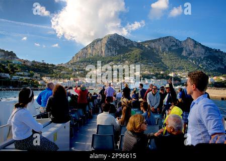 Approaching Capri harbour by boat. Passengers on the top deck of the scheduled ferry from Alamlfi arriving. Capri is an island located in the Tyrrhenian Sea off the Sorrento Peninsula, on the south side of the Gulf of Naples in theCampaniaregion of Italy  Capri, is famed for its rugged landscape, cultural history, upscale hotels and shopping Stock Photo