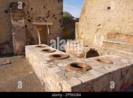 Herculaneum uncovered. Herculaneum was buried under volcanic ash and pumice in the eruption of Mount Vesuvius in AD 79. Ercolano, Campania, Italy . Remains of a shop sellingfrom large ceramic pots. Possibly a  tavern/ bar with pottery vats for beverages Stock Photo