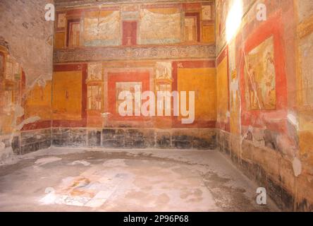 Interior room with painted walls in a house in Pompei. Pompeii was buried under meters of ash and pumice after the catastrophic eruption of Mount Vesuvius in 79 A.D. The preserved site features excavated ruins of streets and houses that visitors can freely explore. Stock Photo