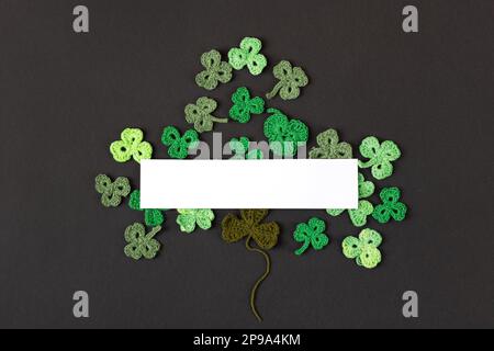 St Patrick's Day concept. Composition made of knitted green shamrocks in the form of three-leaf clover on a black background. Holiday sign and knitted Stock Photo