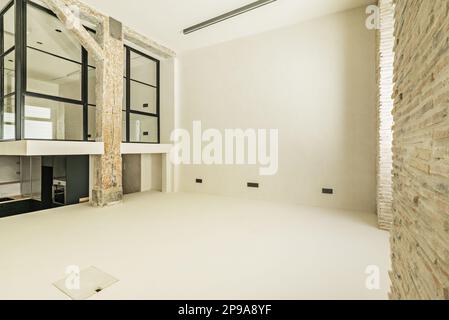 Spacious empty loft with a metal and glass enclosure, polished white concrete floors and walls of a loft with old wooden columns and beams Stock Photo