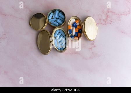 Some metal boxes full of pills and dragees on a pink marble surface Stock Photo