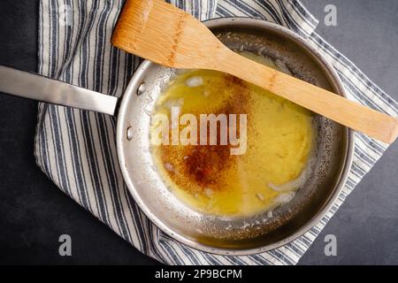 Brown Butter in a Stainless Steel Skillet with a Wooden Spatula: Overhead view of browned butter in a frying pan on a kitchen towel Stock Photo