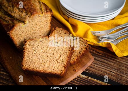 Sliced Banana Bread on a Wooden Cutting Board: Slices of freshly made banana bread with plates and forks in the background Stock Photo