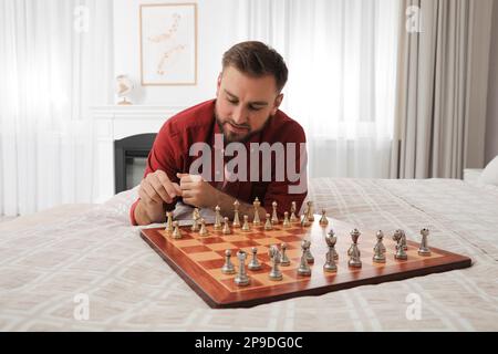 Young man playing chess alone on bed at home Stock Photo