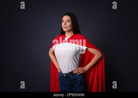 Confident young woman wearing superhero cape on grey background Stock Photo
