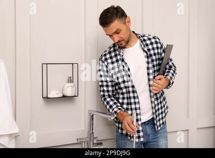 Plumber with clipboard checking water tap in bathroom Stock Photo