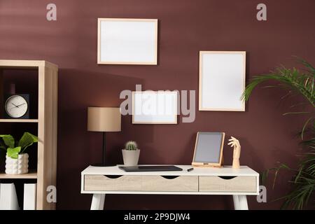 Empty frames hanging on brown wall indoors. Mockup for design Stock Photo
