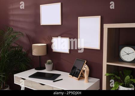 Empty frames hanging on brown wall indoors. Mockup for design Stock Photo
