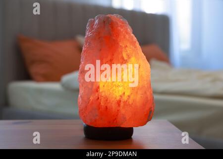 Himalayan salt lamp on wooden table in bedroom Stock Photo