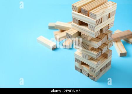 Jenga tower and wooden blocks on light blue background, space for text Stock Photo