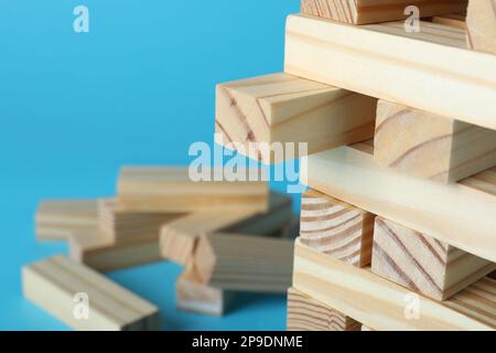 Jenga tower made of wooden blocks on light blue background, closeup. Space for text Stock Photo