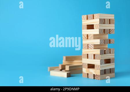 Jenga tower and wooden blocks on light blue background, space for text Stock Photo