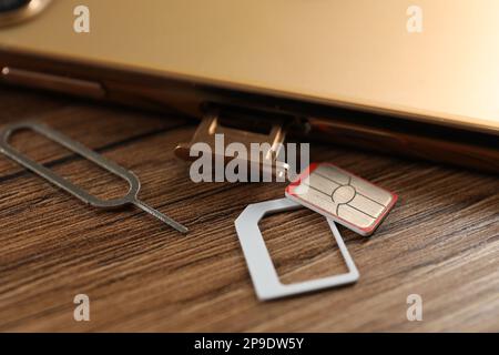 SIM card, mobile phone and ejector tool on wooden table, closeup Stock Photo