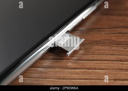 Mobile phone with Sim card in tray on wooden table, closeup Stock Photo