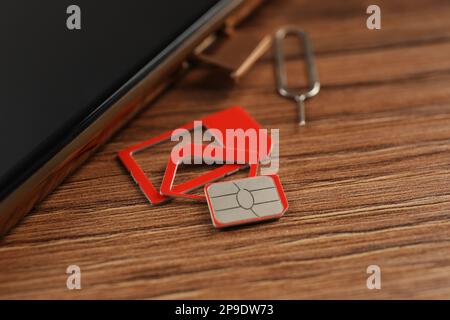 SIM card, mobile phone and ejector tool on wooden table, closeup Stock Photo