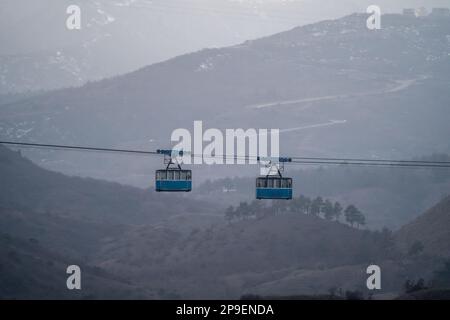 Two blue public old cabins of cable car moves against backdrop of misty ...