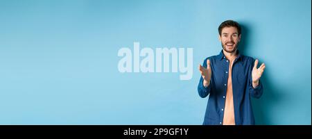 Cheerful young man pointing hands at camera and smiling, feeling glad for you, praising nice work, standing on blue background Stock Photo