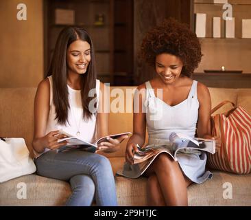 theres always a way to keep busy. two friends sitting on a sofa reading through magazines. Stock Photo