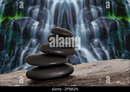 Massage stones on stone underground in front of a waterfall Stock Photo