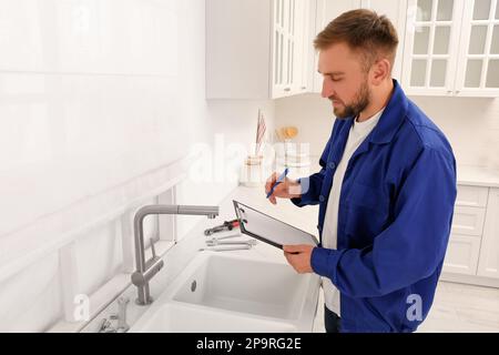 Plumber with clipboard checking water tap in kitchen Stock Photo