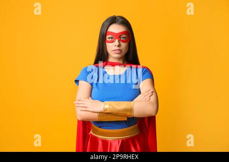 Confident young woman wearing superhero costume on orange background Stock Photo